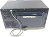 The back of a black Samsung microwave oven is shown, with its power cord plugged in and coiled on the floor. Produktbild-Vorschau