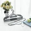A set of grey plastic clothes hangers is displayed on a white surface next to a vase of white flowers. Náhled obrázku produktu