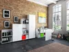 A modern office space with a brick wall, large windows, and a white modular shelving and desk unit. Produktbild-Vorschau