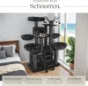 A multi-level cat tree with various platforms, a hideaway, and scratching posts, set up in a room with a bed and a window view of the ocean. Náhled obrázku produktu