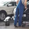 A person in blue overalls is working on a car with a black extension cord reel nearby. Podgląd zdjęcia produktu