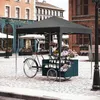 A flower cart is set up under a black canopy on a cobblestone street in front of buildings. Produktbild-Vorschau