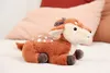 A plush toy deer with a star projector on its back, lying on a white surface with pillows in the background. Produktbild-Vorschau