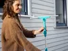 A woman is holding a window cleaning tool outside a house. Produktbild-Vorschau