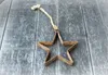 A rustic star ornament made of metal with a rope hanger, placed on a weathered wooden surface. Produktbild-Vorschau