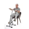 An elderly man is sitting on a chair and using a pedal exerciser. Produktbild-Vorschau