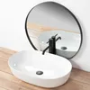 A white oval countertop sink with a black faucet is shown in front of a round mirror reflecting the sink and faucet. The products are placed on a wooden floor. Anteprima dell’immagine prodotto