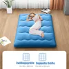 A woman is sleeping on a blue floor mattress in a room. Produktbild-Vorschau