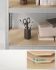 A close-up view of a shelf in a storage unit, showing a pencil holder with scissors and brushes, and stacked boxes. Náhled obrázku produktu
