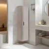 A tall, narrow beige cabinet with a fluted design stands against a tiled wall in a modern bathroom. Produktbild-Vorschau