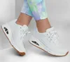 A pair of white Skechers sneakers on a person's feet, with colorful tie-dye pants. Anteprima dell’immagine prodotto