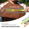 A person is stretching a green silicone band, with a ruler graphic indicating tensile length, and other colored bands are shown in the foreground. Produktbild-Vorschau