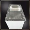 A stainless steel kitchen sink with a draining board is shown from a slightly elevated angle, placed on top of a white cabinet. Produktbild-Vorschau