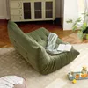 A green sofa chair with a blanket and a book on it, placed on a rug in a living room. Produktbild-Vorschau