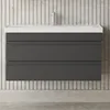 A modern bathroom vanity with a white countertop and dark gray drawers, set against a tiled wall. Produktbild-Vorschau