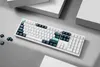 A white mechanical keyboard with dark blue and teal keycaps, arranged on a light gray surface with white geometric shapes in the background. Voir les images du produit