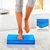 A person's legs and feet are shown stepping onto a blue balance pad in a bright, clean room. Produktbild-Vorschau