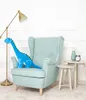 A blue dinosaur plush toy sits on a light blue armchair next to a floor lamp and small side tables. Anteprima dell’immagine prodotto