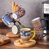 Bunte Tassen hängen an Holzhänger oder stehen auf Holz, dazu Kaffee und Keksen. Náhled obrázku produktu