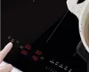 A close-up of a person's finger touching the control panel of a black induction cooktop. Digital displays show cooking settings. Produktbild-Vorschau