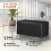 A black storage box is placed in a modern, well-lit indoor space with large windows and plants. Produktbild-Vorschau