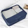 A blue fabric organizer bag filled with neatly folded clothes, placed on a white bed with pillows. Anteprima dell’immagine prodotto
