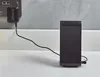 A black Shark brand charger plugged into a wall socket, connected by a black cord to a black charging dock for a cordless vacuum cleaner, resting on a white countertop. Produktbild-Vorschau
