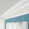 A close-up view of white crown molding against a blue wall. Produktbild-Vorschau