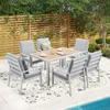 An outdoor dining set with chairs and a table is placed on a patio next to a swimming pool, with a wooden fence and greenery in the background. Produktbild-Vorschau