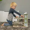 A young boy is playing with a wooden toy garage on a carpeted floor. Produktbild-Vorschau