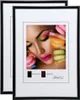 Two black picture frames are shown, one slightly behind the other. The front frame displays a close-up image of a woman's face with colorful makeup and macarons. Text indicating frame sizes and a brand logo are visible below the image. Produktbild-Vorschau