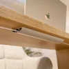 A close-up view of a cable management channel attached to the underside of a wooden shelf, with a white cable running through it. A laptop is visible on the shelf above. Anteprima dell’immagine prodotto