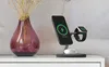A charging station with a phone and smartwatch is placed on a white surface next to a vase with dried flowers. Produktbild-Vorschau