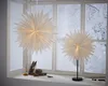 Two white paper star lanterns are displayed on a windowsill with a snowy winter scene visible through the window. Podgląd zdjęcia produktu