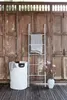A white towel ladder with a gray towel draped over it, a white laundry basket with a gray towel, and a vase with pink flowers are placed in front of a rustic wooden door. Produktbild-Vorschau