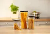 Three clear plastic food storage containers filled with different types of pasta are arranged on a wooden countertop in a kitchen setting. Produktbild-Vorschau