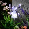 A solar-powered angel garden stake with purple flowers and lights, placed among plants next to a gravestone. Náhľad obrázku produktu