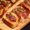 Close-up of bruschetta with prosciutto and herbs on a wooden board. Voir les images du produit