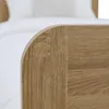 A close-up view of the corner of a wooden bed frame, with white bedding visible in the background. Produktbild-Vorschau