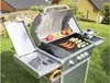 A gas grill with food cooking on it, set up in a backyard. Podgląd zdjęcia produktu