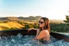 A woman relaxing in a hot tub with a scenic view of hills and trees. Náhled obrázku produktu