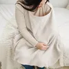 A woman is sitting on a bed, using a nursing cover. Produktbild-Vorschau
