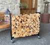 A metal firewood rack filled with logs is placed on a stone patio in front of a stone building with wooden doors. Produktbild-Vorschau
