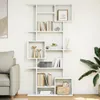A white, modern, modular bookshelf filled with books and decorative items, placed in a living room setting next to a sofa and a large plant. Náhľad obrázku produktu