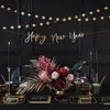 A table setting for a New Year's Eve celebration with a floral arrangement, candles, and festive decorations. Produktbild-Vorschau
