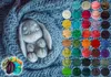 A felted bunny is nestled in a blue knitted blanket, surrounded by colorful balls of wool. Produktbild-Vorschau