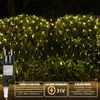A net of fairy lights is draped over a bush at night, with a power adapter in the foreground. Produktbild-Vorschau