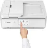 A hand is shown pressing a button on the touchscreen of a white Canon printer. Podgląd zdjęcia produktu