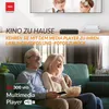 An older couple laughing while watching TV, with a media player on a shelf in the background. Produktbild-Vorschau