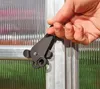A hand is shown operating a latch on a greenhouse door. Náhled obrázku produktu